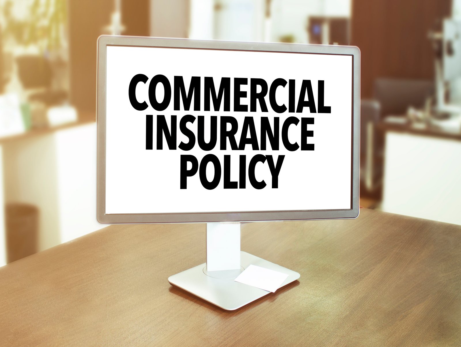 A computer monitor standing on a wooden office desk displaying the text Commercial Insurance Policy