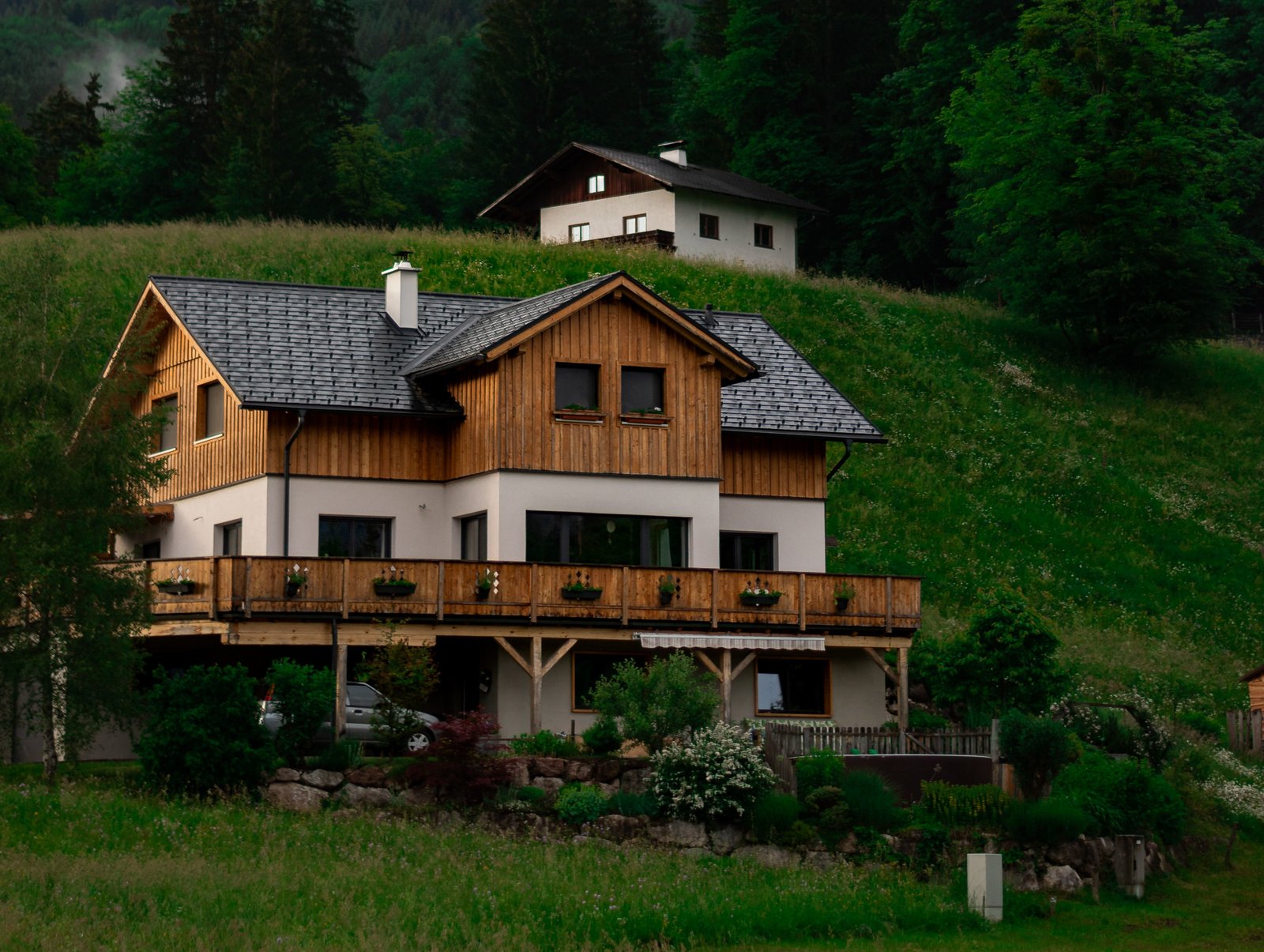 A beautiful multi-story wood and plaster house nestled against a green alpine hillside